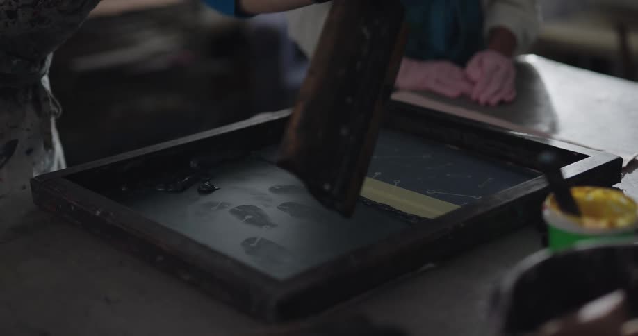 Two people are laying fabric over a silk screen that has been loaded with ink