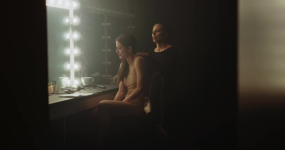 Two women talk in a dressing room and then the older woman rubs the younger womans shoulders