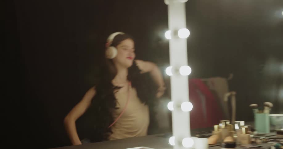 A woman in a room with headphones dancing with a wall and mirror in the background