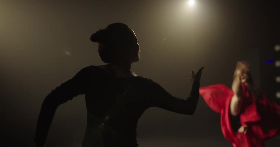 A dancer in red dress performs on a stage as another gives her direction