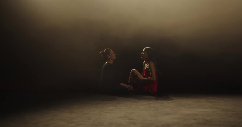 Two women sit on a stage as they talk then clasp hands