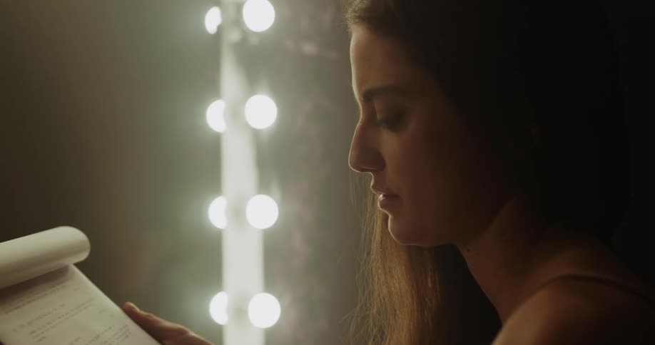 A woman in a room looking at a notebook with lights and a mirror in the background