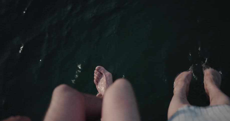 Two people are sitting above water and splashing their feet in the water