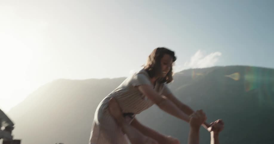 A woman and a man attempt a difficult couples yoga pose on a dock on a lake in the mountains