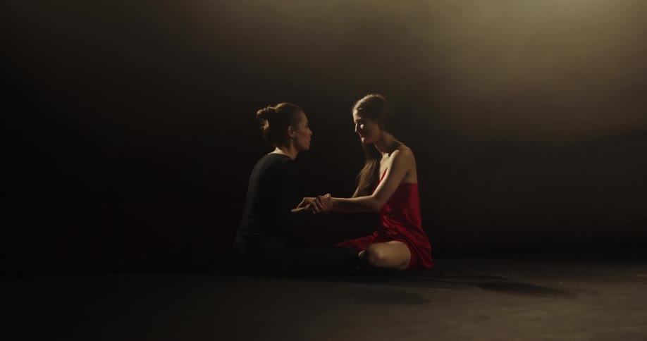 Two dancers sit on a stage and talk and hug