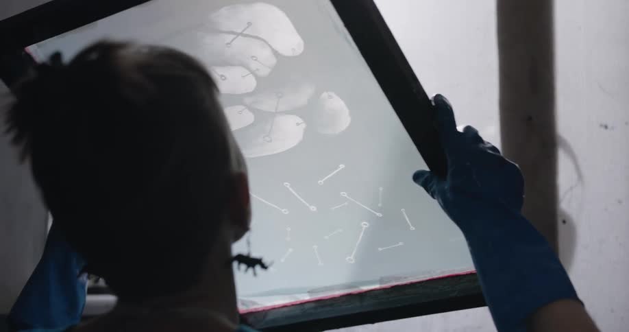 A woman with gloves in a room holding up a picture frame with a wall in the background