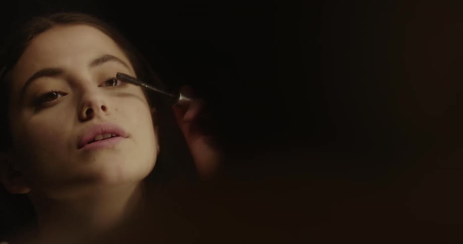 A woman is looking in a mirror and putting on makeup