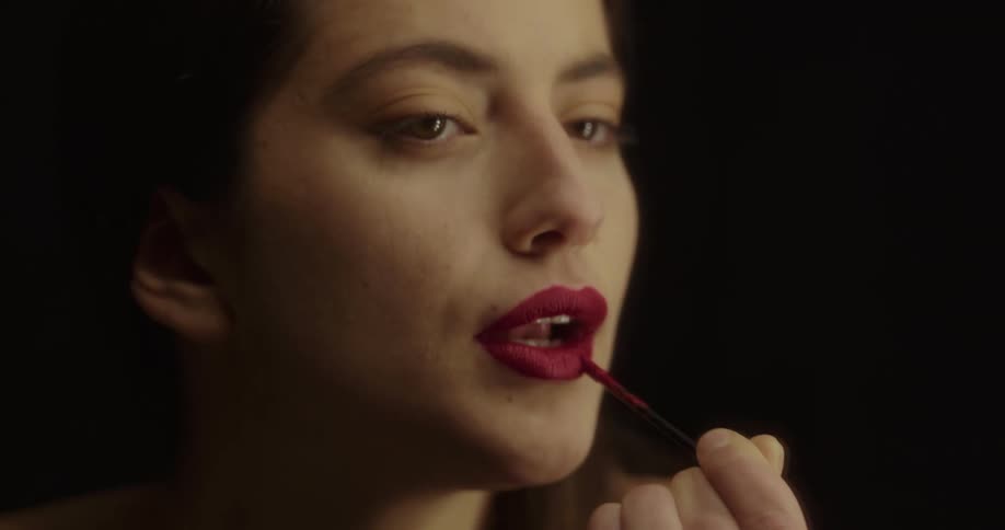 A woman is in a room and putting lipstick on