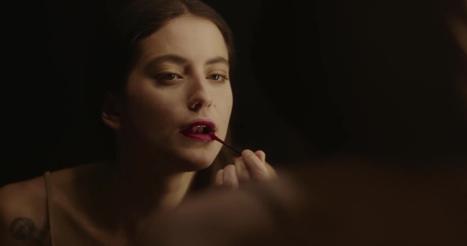 A woman is looking in a mirror and applying lipstick