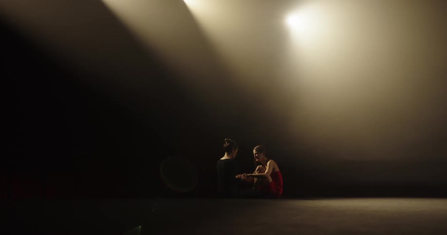 Two women sit on a stage and one comforts the other then they hug