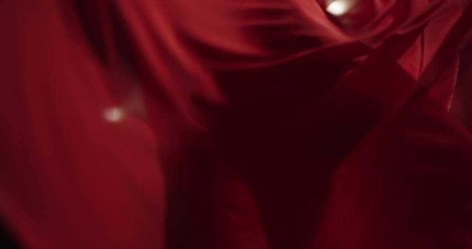 A woman in tight red dress with sheer veil twirls with outstretched arms