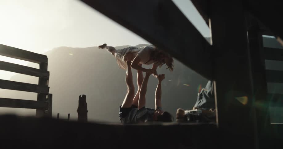 A man lies on the ground with his feet in the air and pushes them against a womans stomach as he supports her so she is lying above him