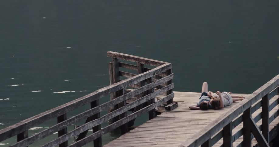 Two people cuddle together at the end of a pier on a lake
