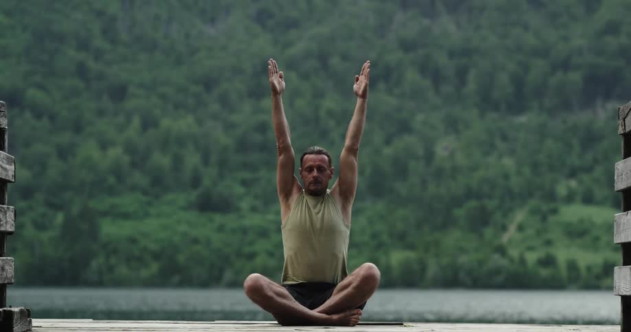 A man raises his arms up and down as he meditates on a pier over a lake