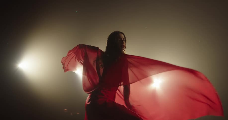 A woman in a flowing red dress is dancing on a smoky stage