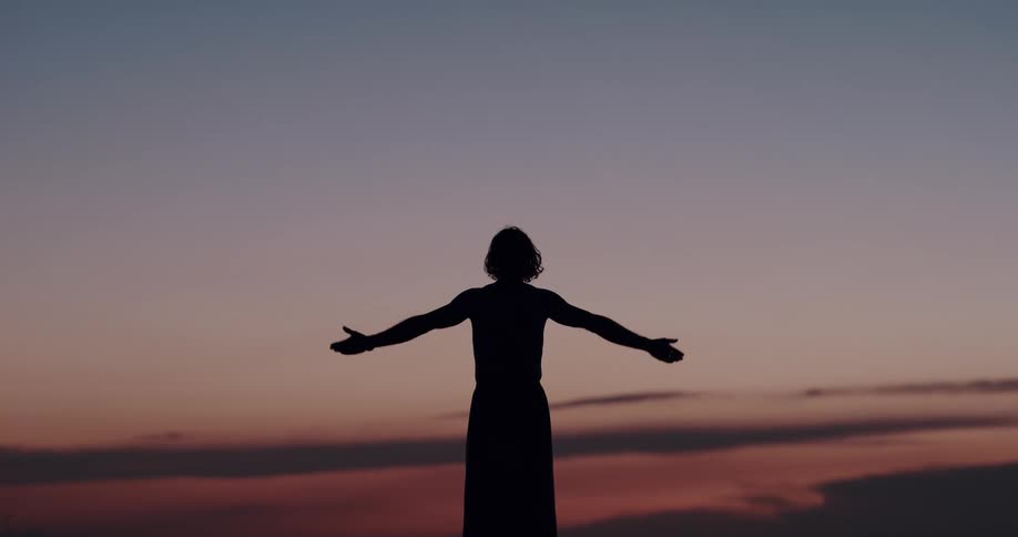 A person stretches hands upwards as the sun is setting
