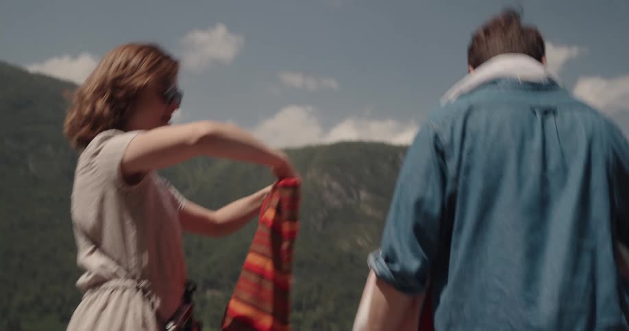 Couple runs and lays towels on pier to swim next to lake with mountains in the background