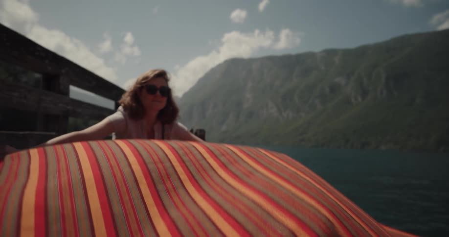 A woman shakes out a blanket then lays it on the deck and crawls onto it