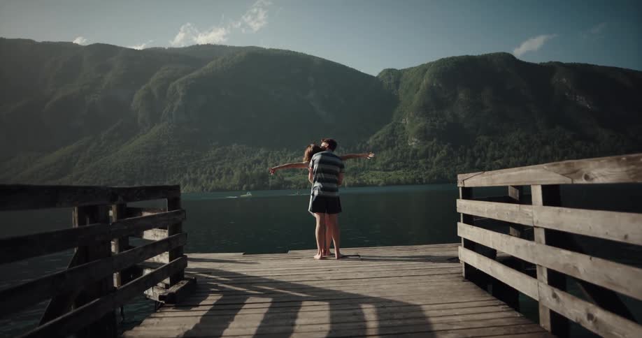 Two people stand at the end of a pier on a lake