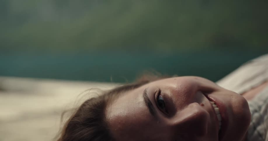 A young woman lies on her back outside and smiles as she turns her head