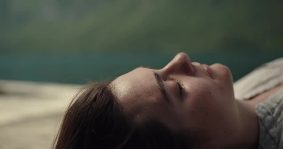 The wind blows the hair of a sleeping woman before she wakes turns her head and smiles