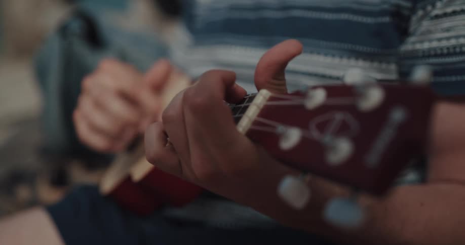 A man plays the ukulele while sitting outdoors during the day