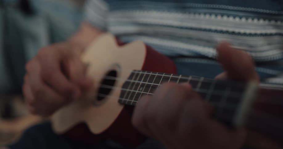 Person wearing striped shirt sits playing an ukulele