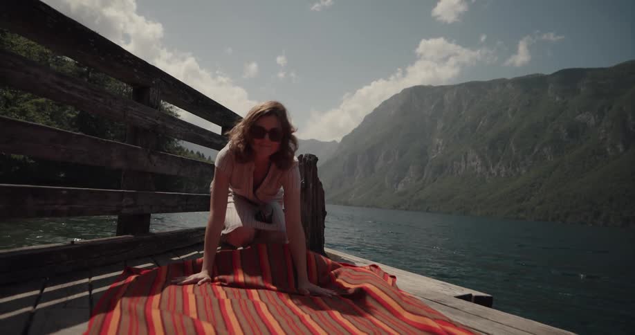 A woman laying down a blanket outdoors near a lake