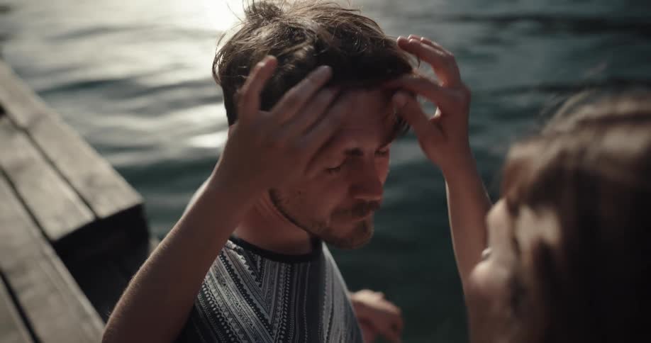Woman runs her fingers through a mans hair then kisses him while they stand near a lake