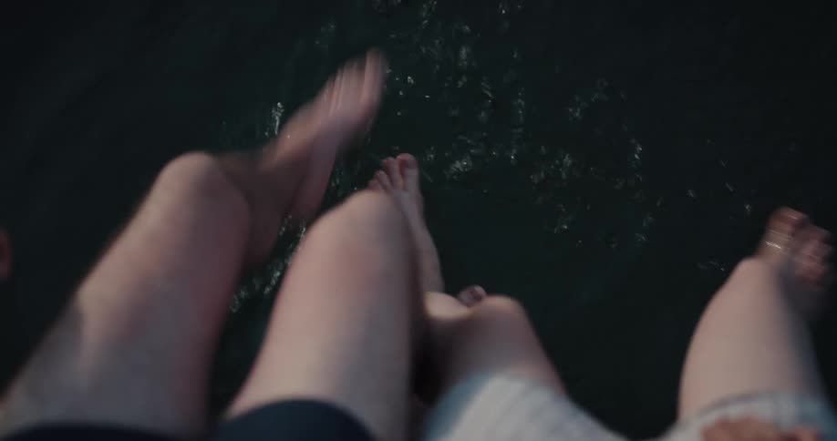 A man and woman are sitting next to each other and playfully splashing their feet in water