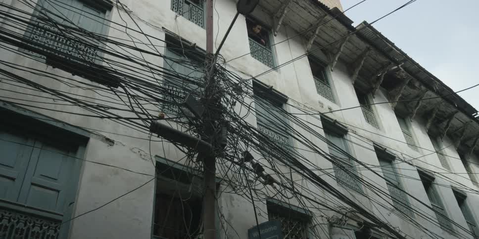 Many tangled wires on a pole in front of a building
