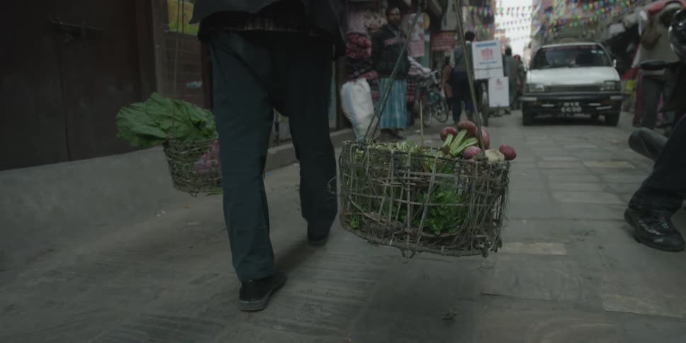 A person carries two baskets as they walk down the street