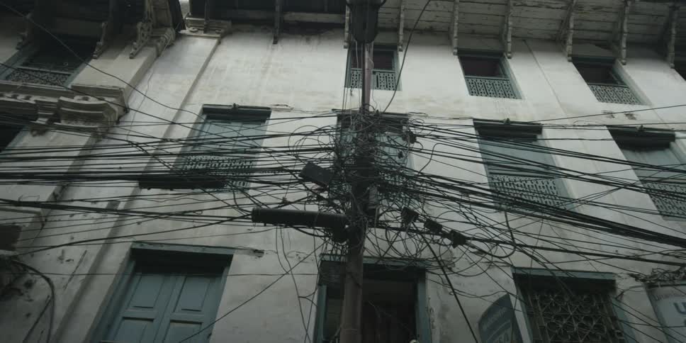 A bunch of cables emerge from a pole in front of an apartment building