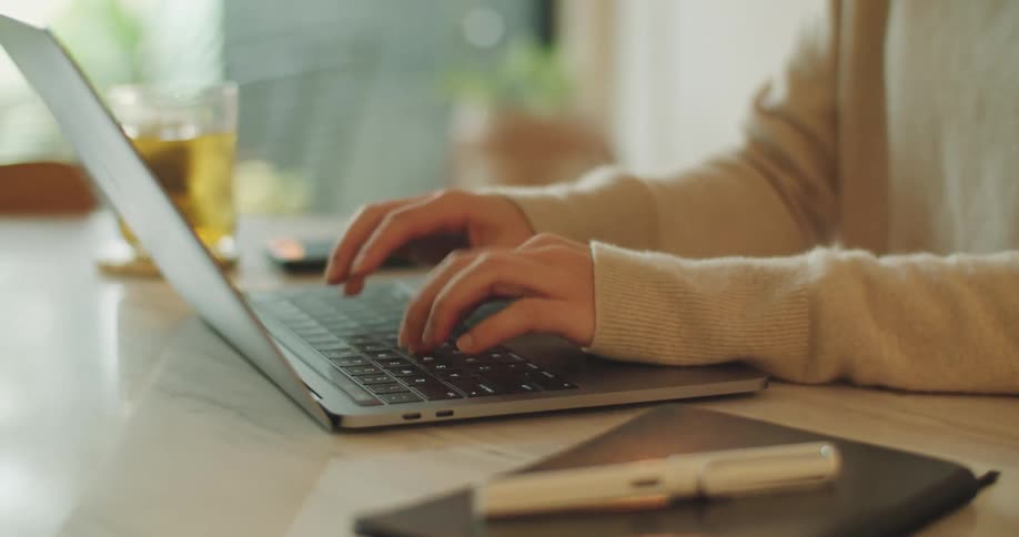Woman with beige sweatshirt sitting at desk types on laptop fast