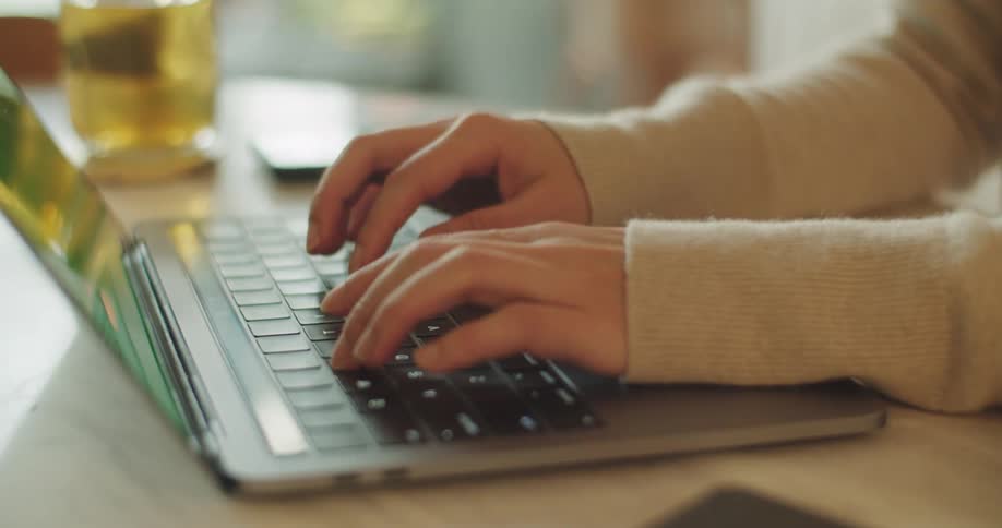 A person is typing fast on a laptop that is on a desk