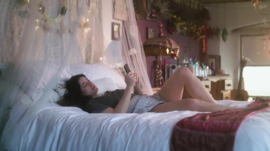 A woman lying on her bed texting and tapping on her phone