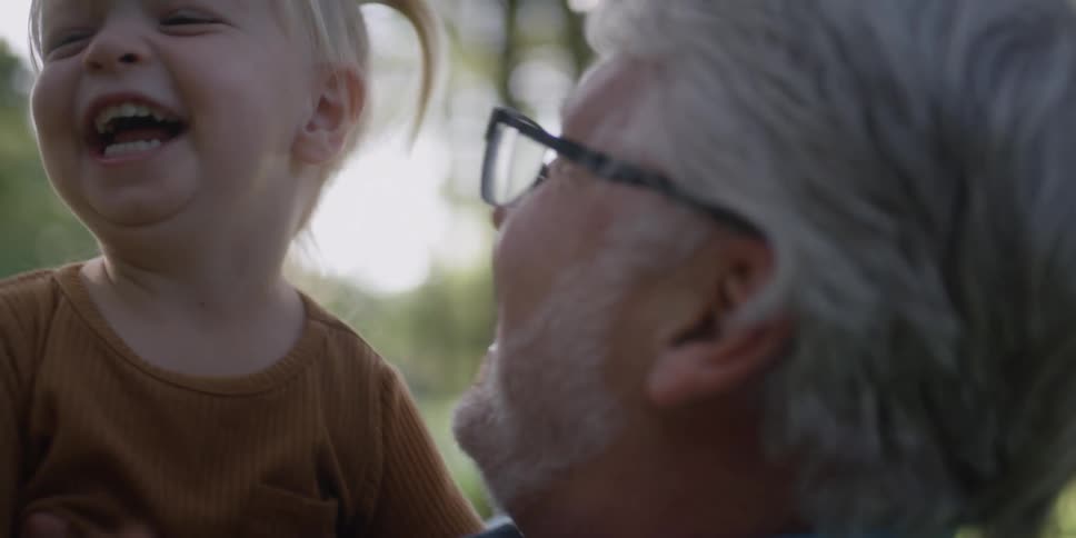 A man holds a young toddler girl outside as they laugh together