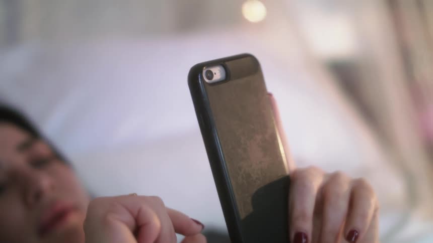 A woman laying in bed looking at her phone