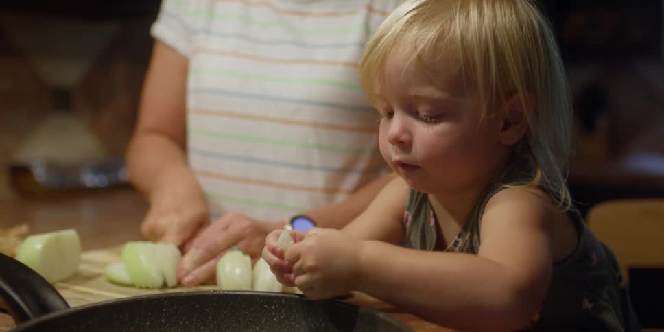 Grandmother cuts onion and granddaughter putting the onion slices in pan in the kitchen