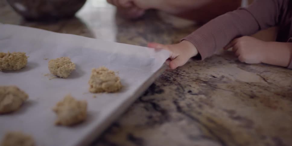 A toddler reaches for the cookie dough balls on a pan on the counter