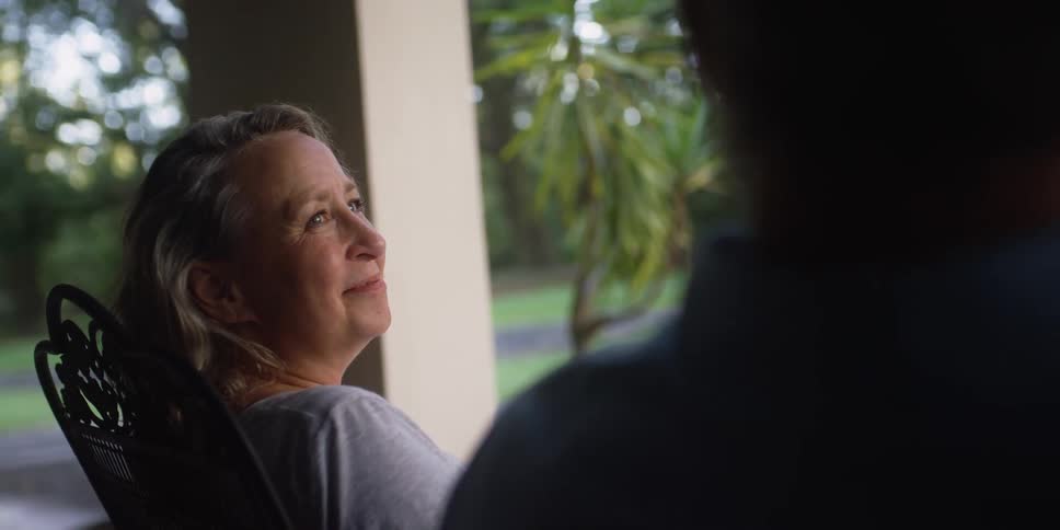 Two people sit on a quiet porch and the woman smiles at the other person