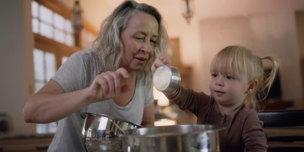 Woman with grey hair and blonde little girl cook in the kitchen