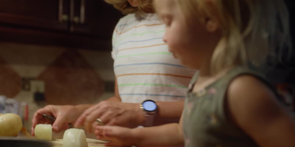 A woman in a kitchen cutting onions with a knife on a cutting board with a girl next to her