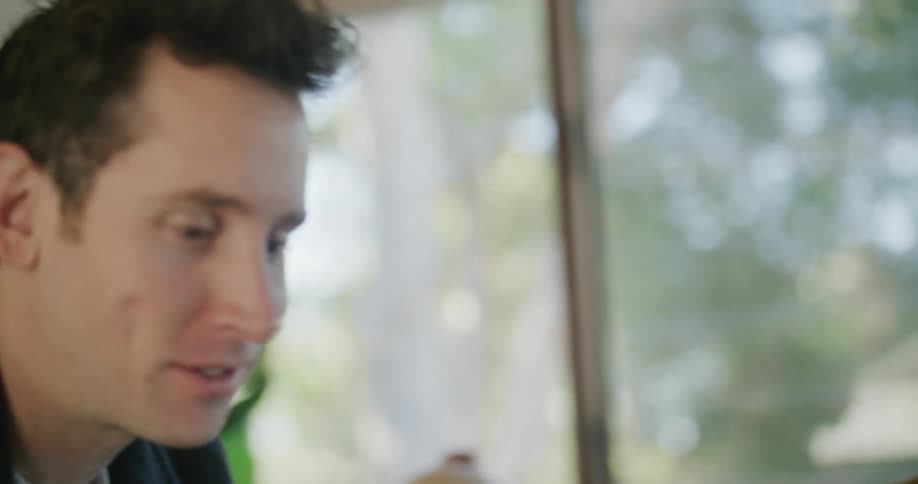 Man and woman smile and laugh as they sit talking near window