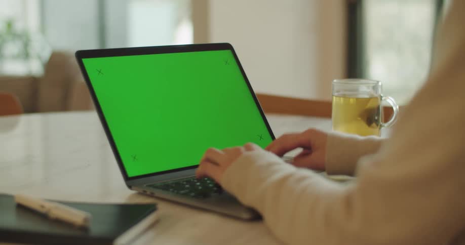 Somebody is sitting at a table typing on a laptop computer with a mug of tea sitting next to the computer
