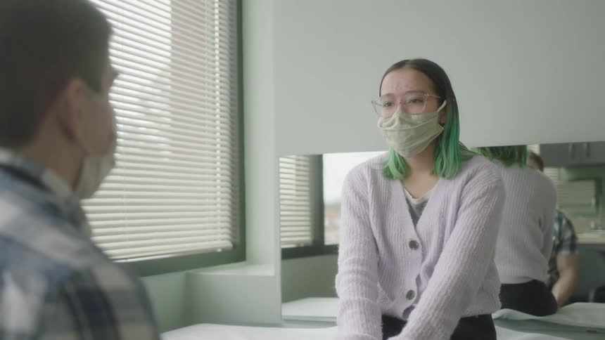Two friends are sitting in a room and talking while wearing face masks