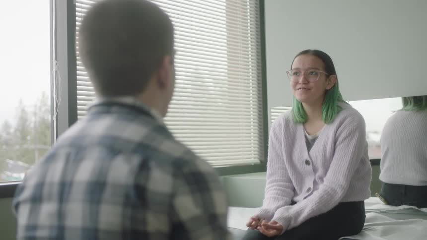 Teenager with green hair sits on an examining table and talks with her doctor