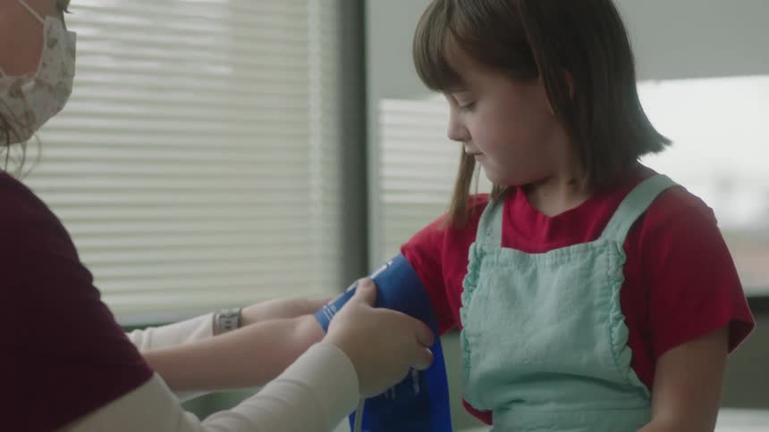 Nurse wraps blood pressure cuff around child patients arm