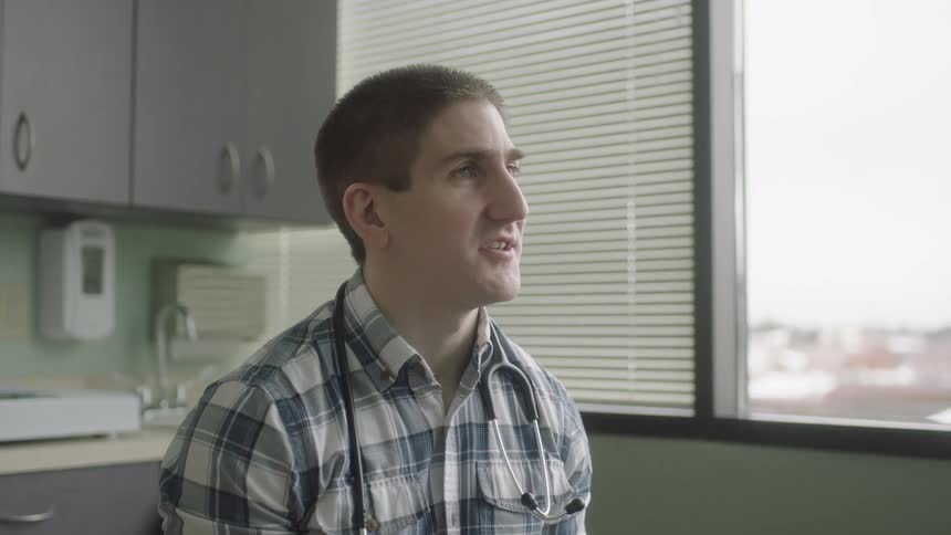 Male doctor wearing stethoscope around neck sits near window talking
