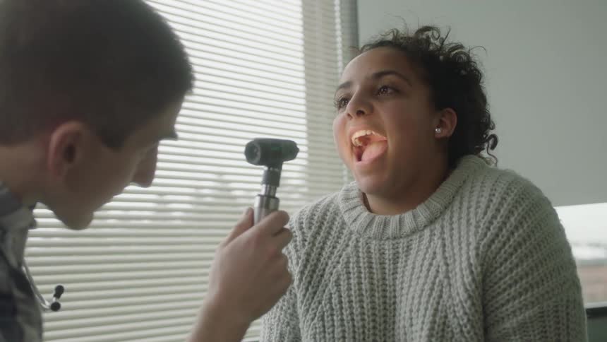 Doctor uses a medical instrument to look in a womans throat